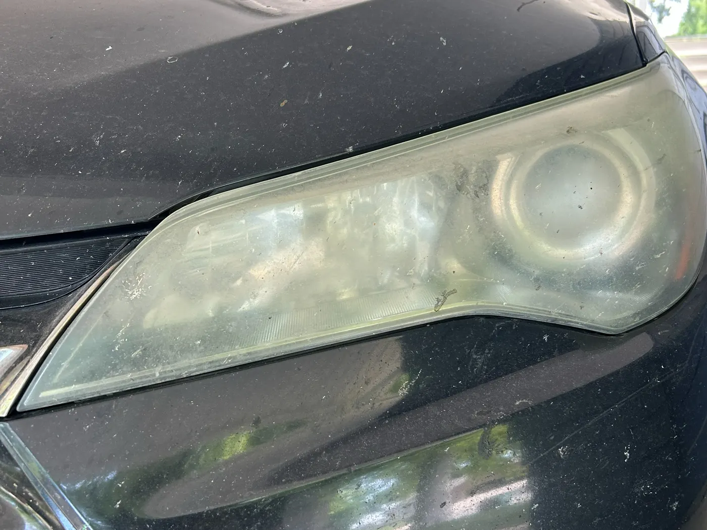 Driver-side headlight on a black Toyota Camry before restoration, heavily oxidized and hazy