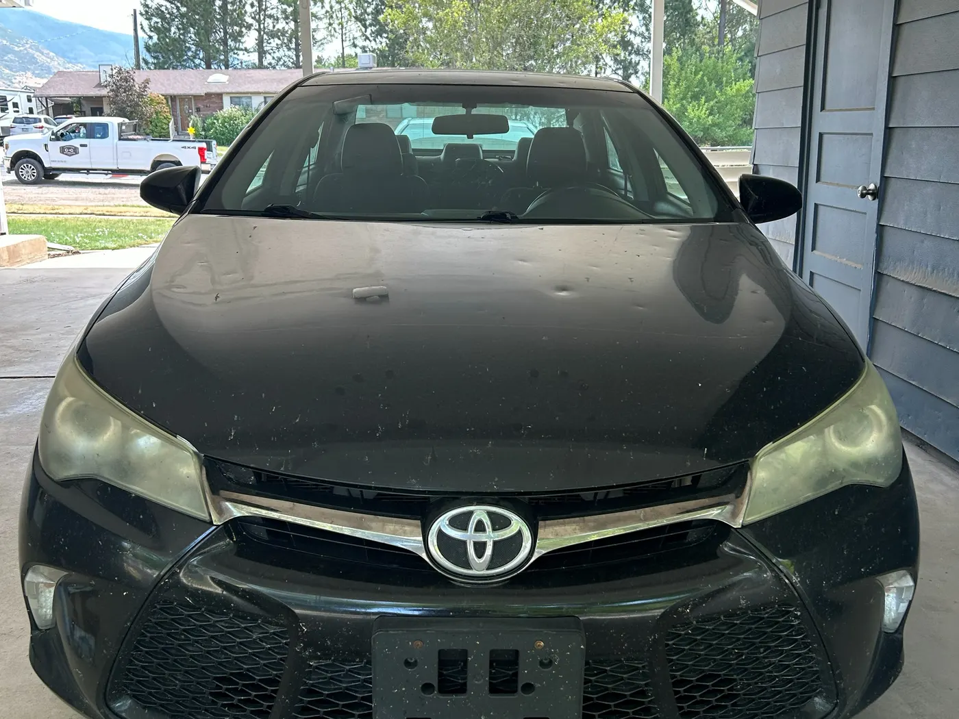 Front of a black Toyota Camry before restoration, both headlights yellowed and dull against the dark paint