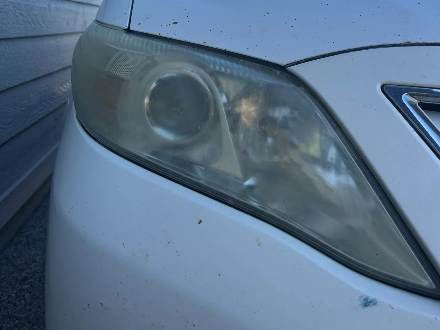 Passenger-side headlight on a white Toyota Camry before restoration, clouded and yellowed at an angle