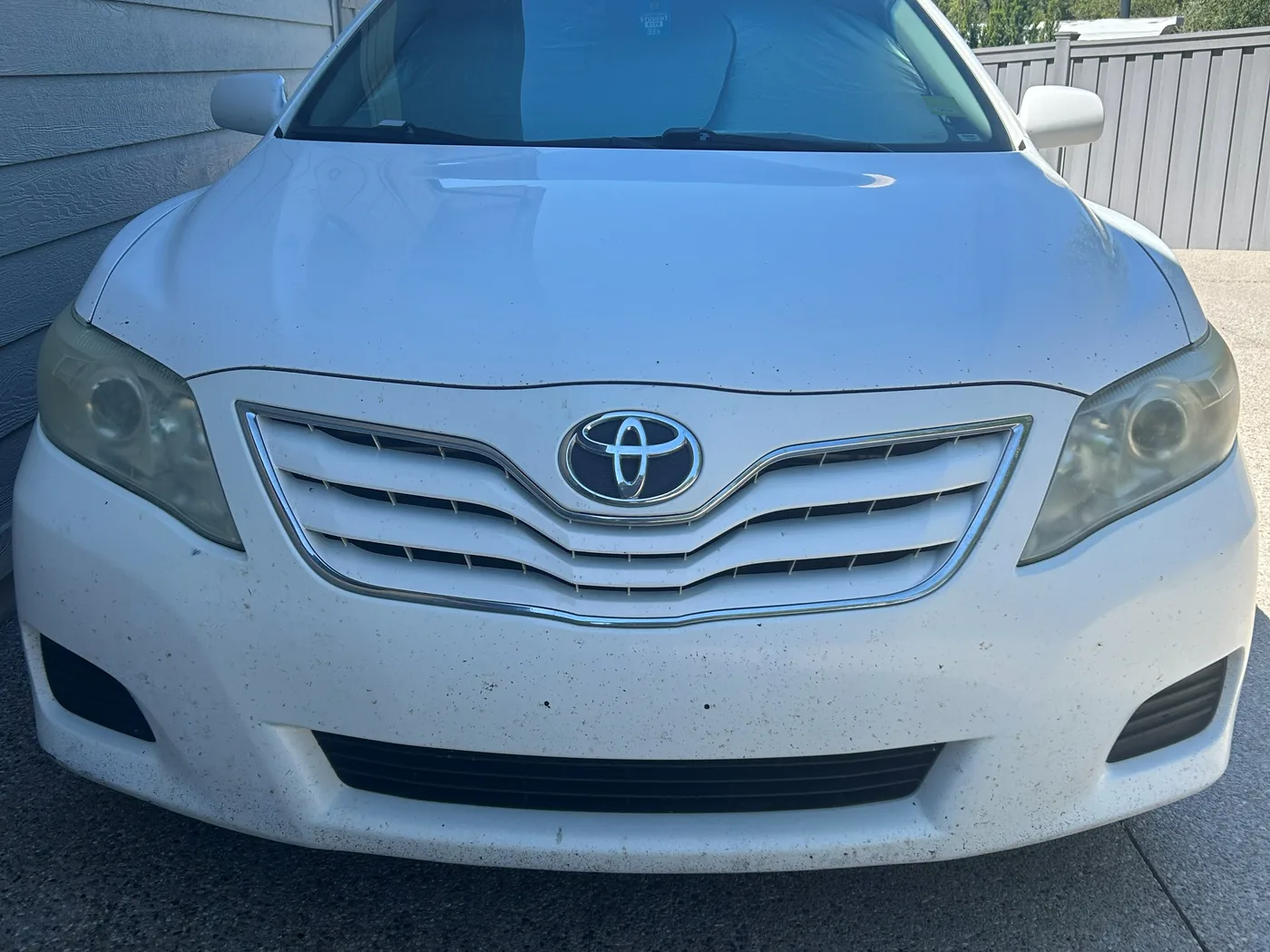 Front of a white Toyota Camry before restoration, both headlight lenses yellowed and hazy
