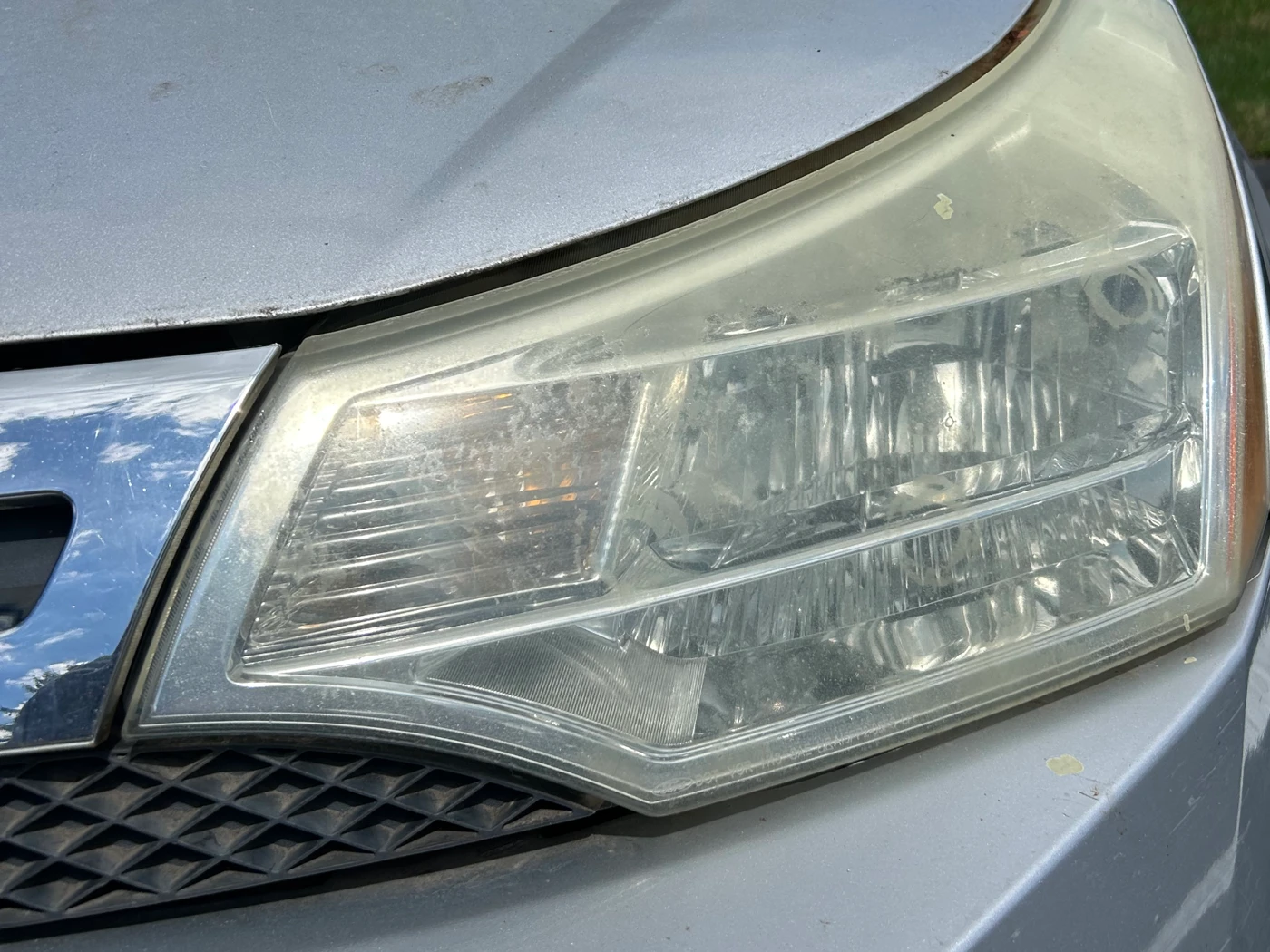 Driver-side headlight on a silver Ford Fusion before restoration, hazed over with a dull yellow film