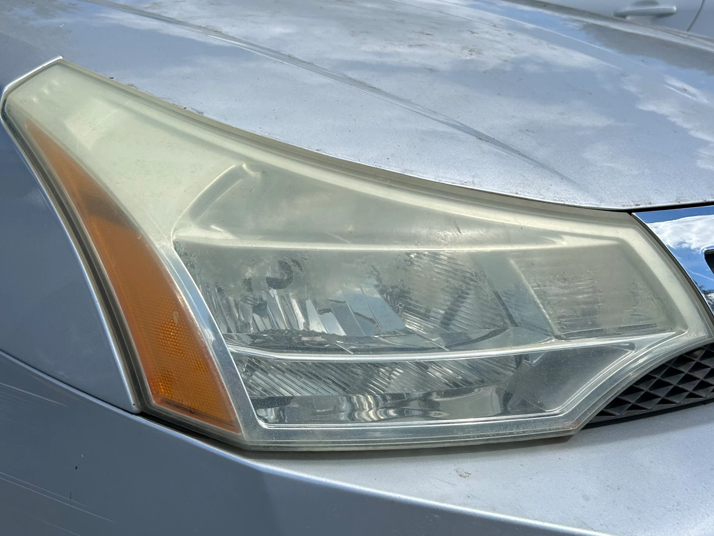 Passenger-side headlight on a silver Ford Fusion before restoration, the lens milky and yellowed across its whole face