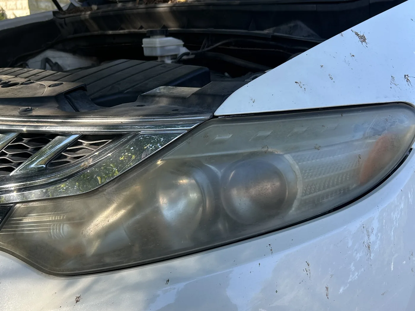 Eye-level view of the same Murano headlight before restoration, the clouded lens dull against the white paint